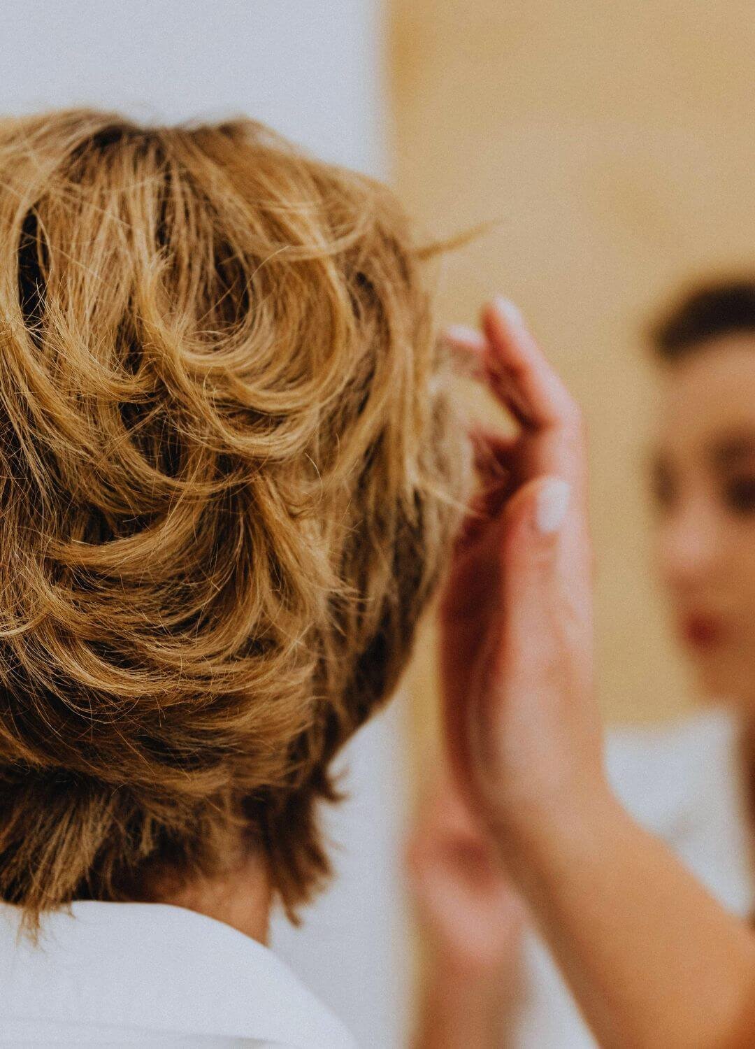 Femme aux cheveux courts se regardant dans le miroir avec une main dans les cheveux