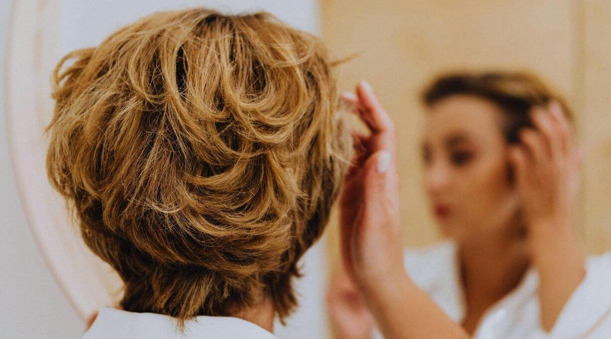 Femme aux cheveux courts se regardant dans le miroir avec une main dans les cheveux
