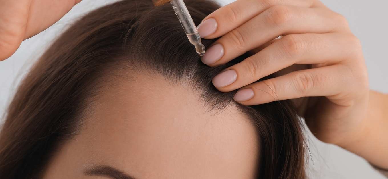 Femme tenant une pipette de sérum pour améliorer la repousse des cheveux qu'elle applique sur son cuir chevelu
