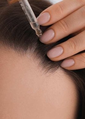 Femme tenant une pipette de sérum pour améliorer la repousse des cheveux qu'elle applique sur son cuir chevelu