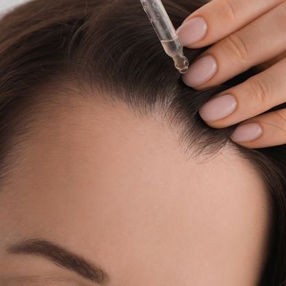 Femme tenant une pipette de sérum pour améliorer la repousse des cheveux qu'elle applique sur son cuir chevelu