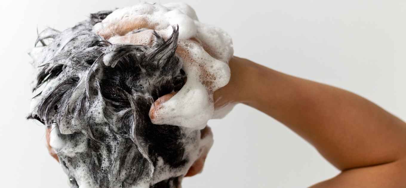 Homme de dos se faisant un shampooing moussant avec une main dans ses cheveux