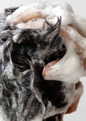 Homme de dos se faisant un shampooing moussant avec une main dans ses cheveux