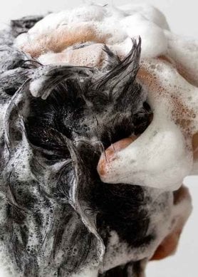 Homme de dos se faisant un shampooing moussant avec une main dans ses cheveux