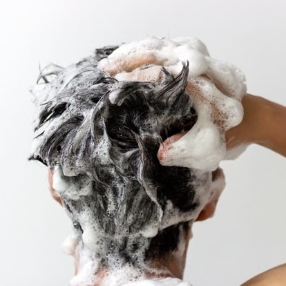 Homme de dos se faisant un shampooing moussant avec une main dans ses cheveux